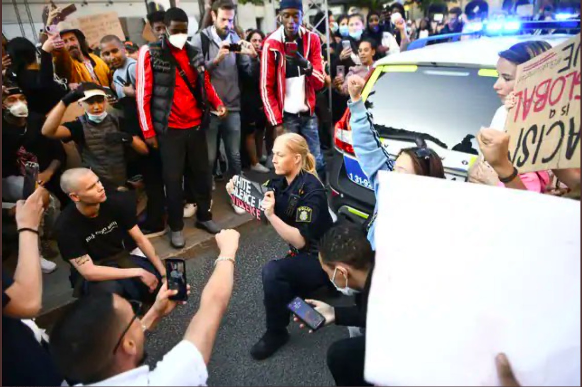 Swedish Police officer holds sign " White Silence in Violence".